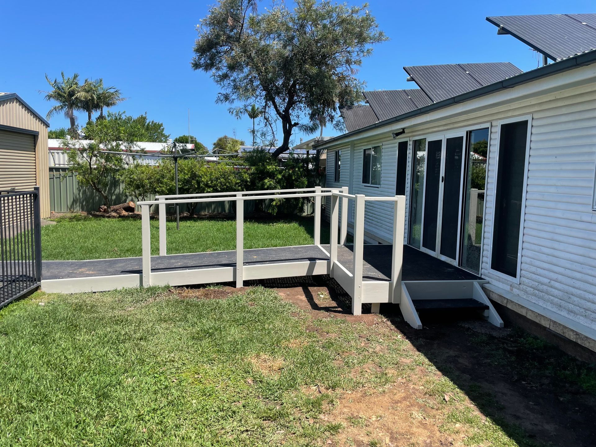 A white house exterior featuring a wooden accessibility ramp leading to a set of glass doors and a small wooden step. - — A1 Maintenance and Building In Old Bar, NSW
