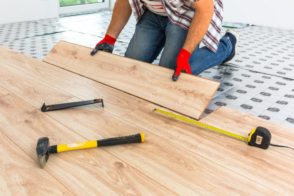 A Man is Installing a Wooden Floor in a Room — A1 Maintenance and Building In Old Bar, NSW