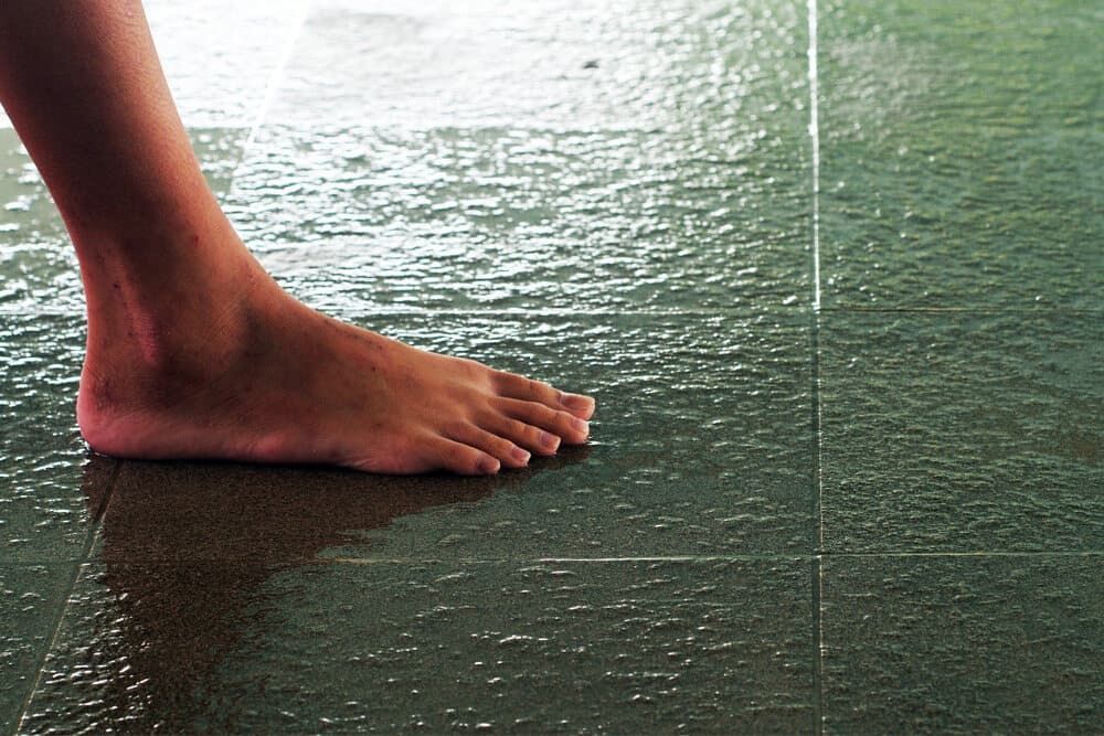 A Person's Bare Foot is Standing on a Wet Tiled Floor — A1 Maintenance and Building In Old Bar, NSW