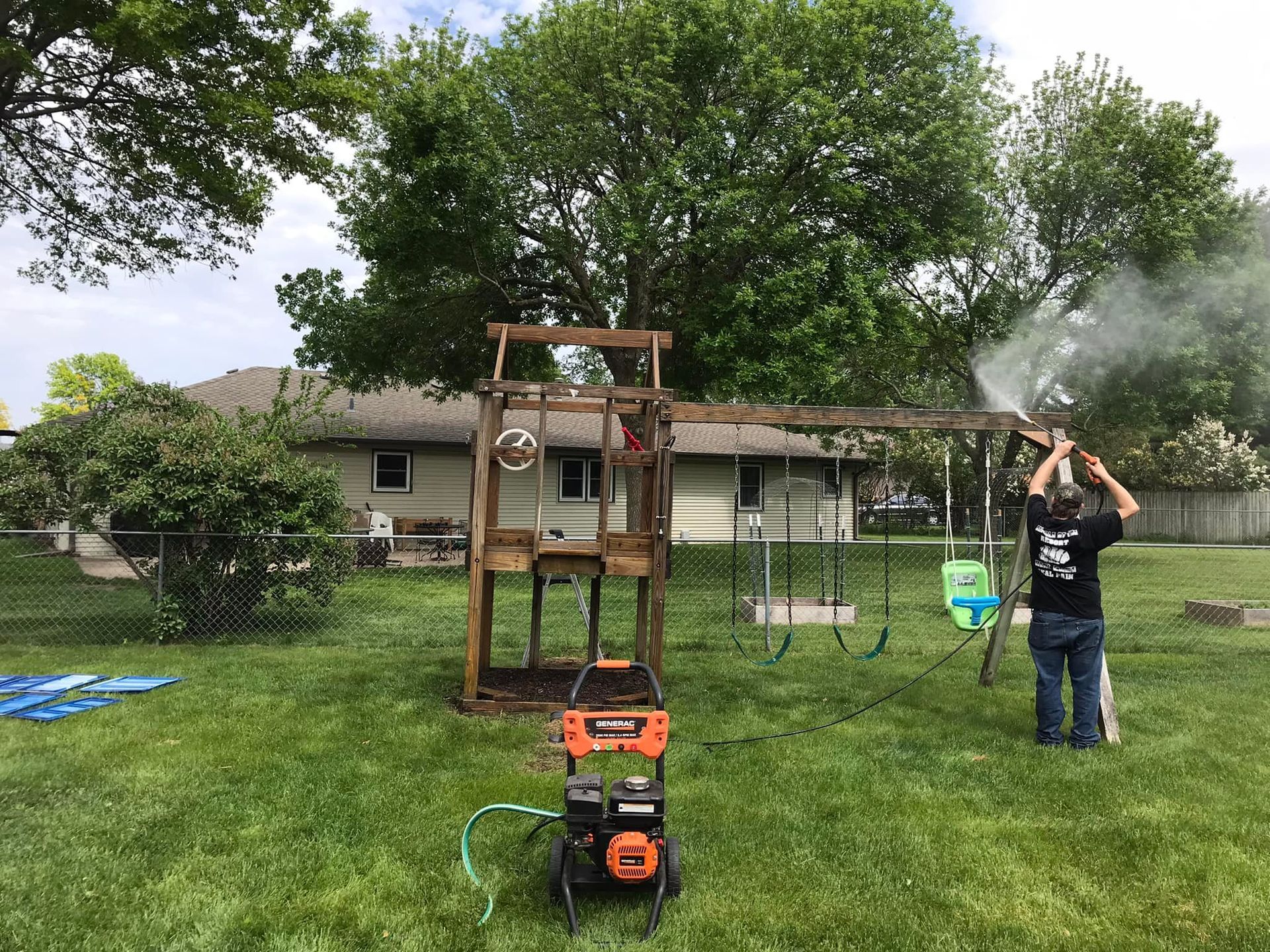 A man is cleaning a wooden swing set in a backyard.