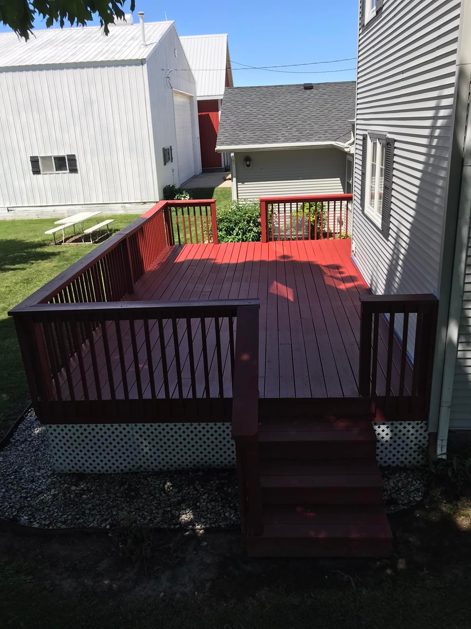 A red deck with stairs is in front of a white house.