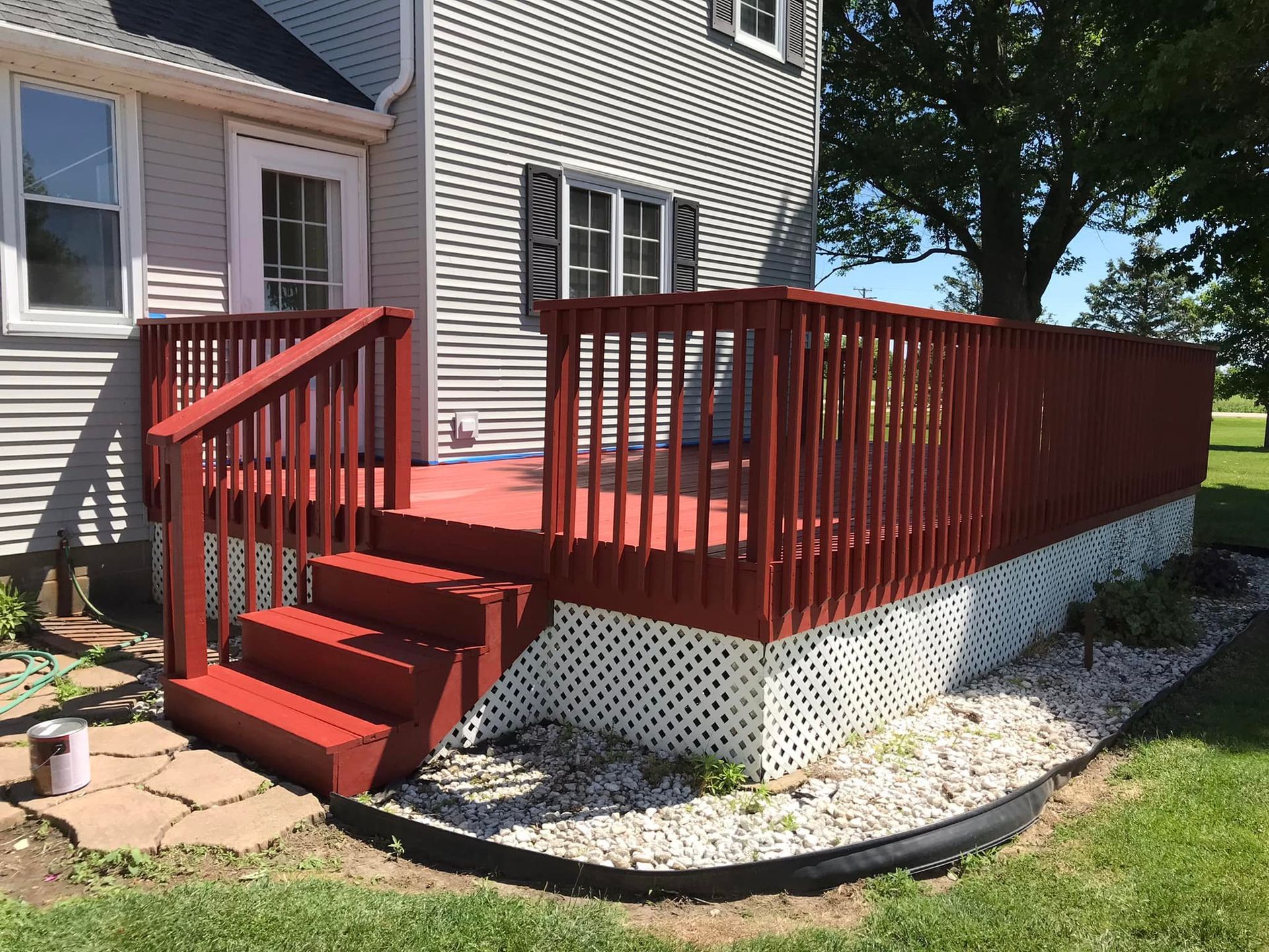 A red deck with stairs is in front of a white house.