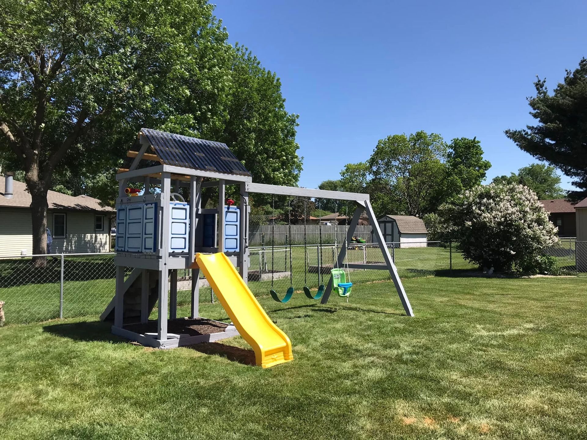 A playground set with a slide and swings in a backyard.