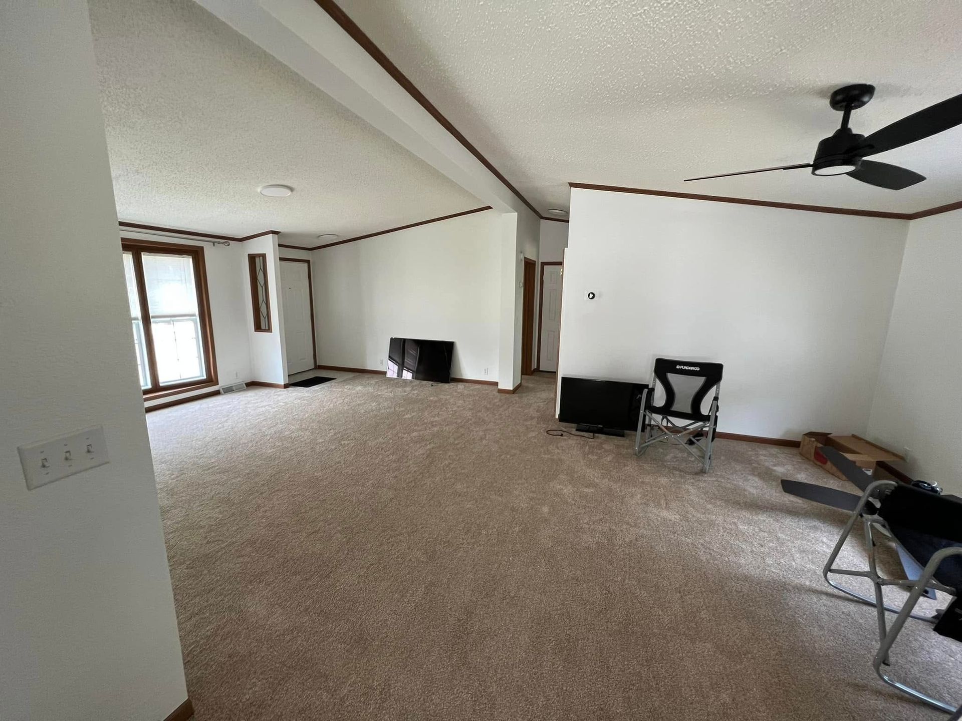 An empty living room with a ceiling fan and a chair.