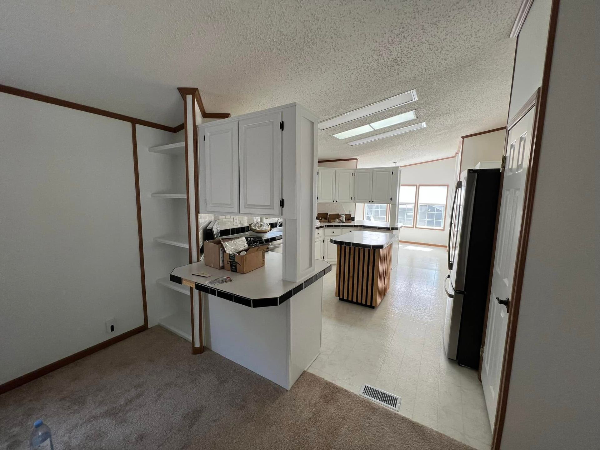 A kitchen in a mobile home with white cabinets and a black refrigerator.