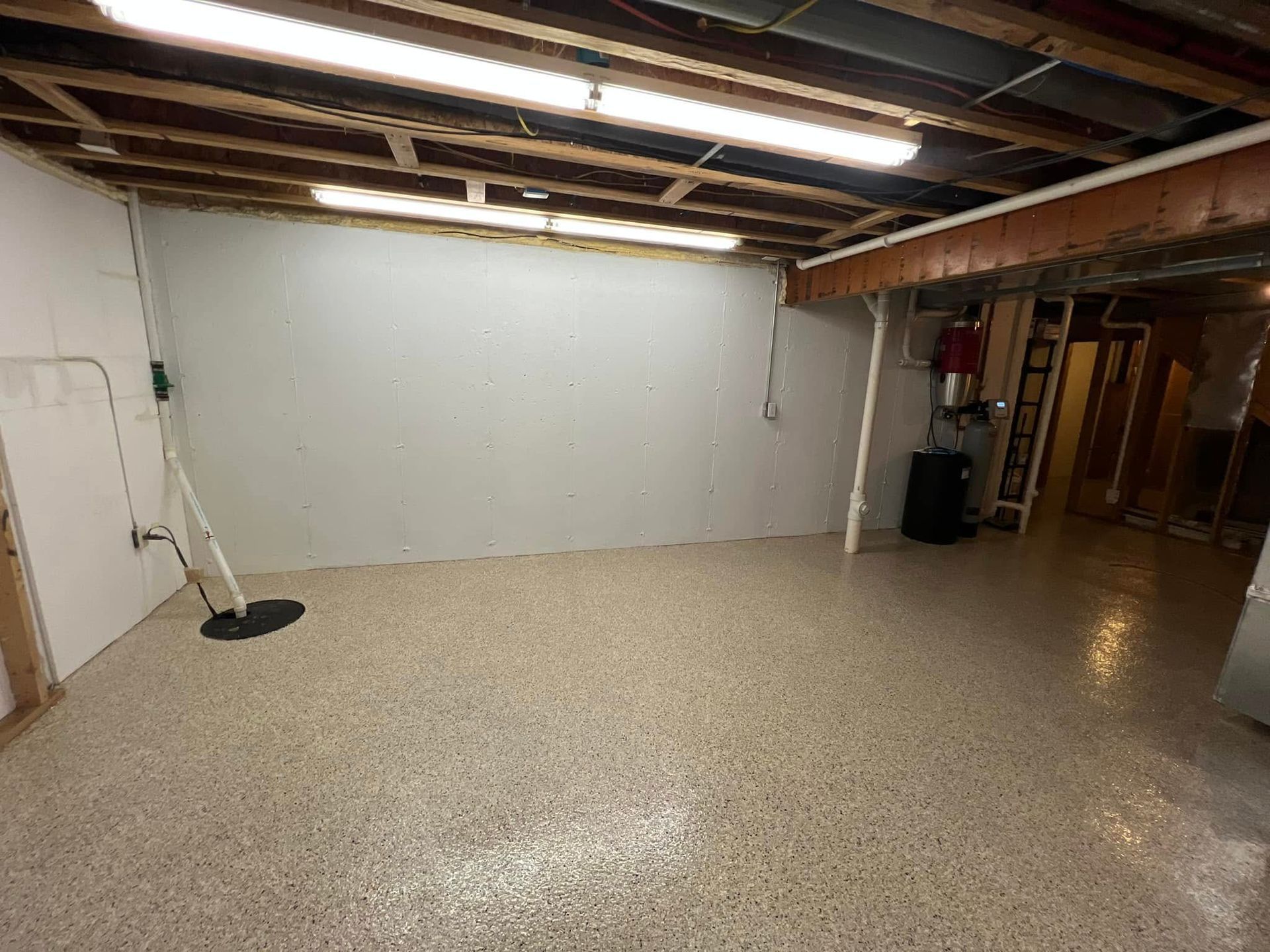 An empty basement with a white wall and a concrete floor.