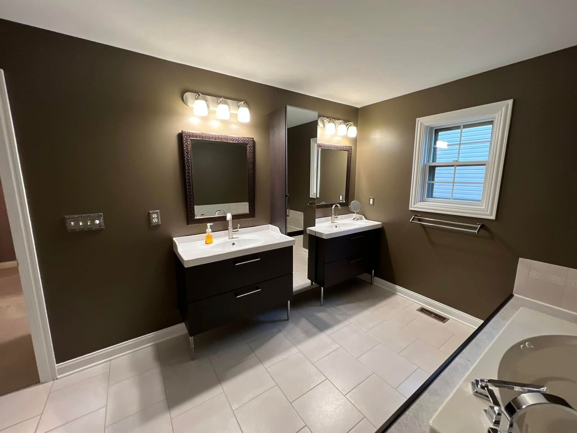 A bathroom with two sinks , two mirrors and a window.