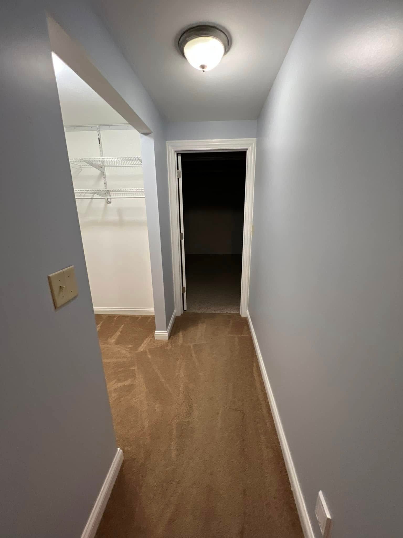 A hallway with a light on the ceiling and a door leading to a dark room.