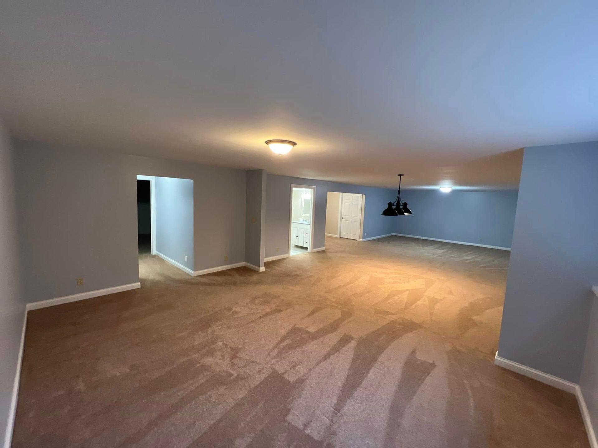 A large empty room with a carpeted floor and a ceiling light.