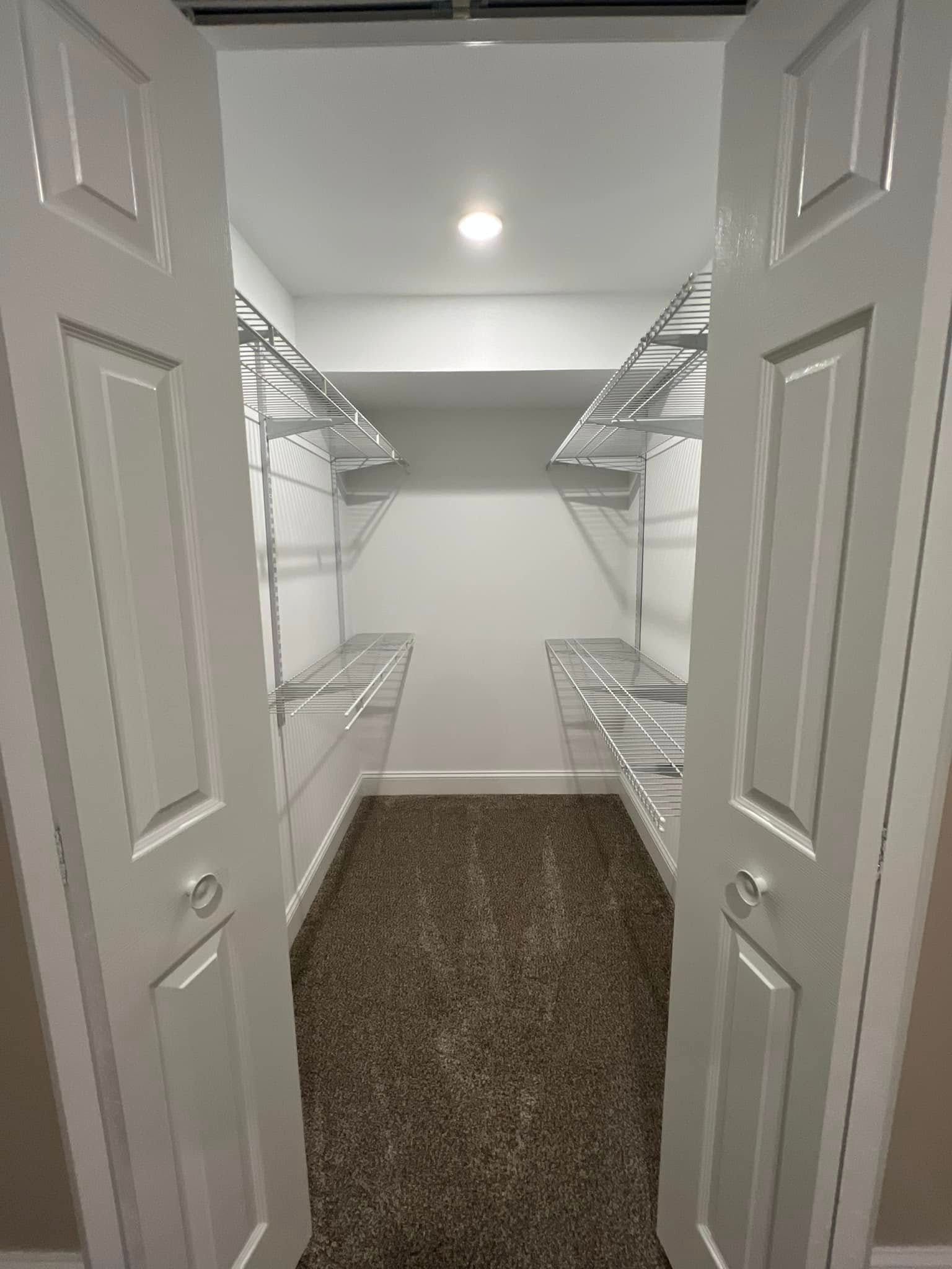 A walk in closet with lots of shelves and a brown carpet.