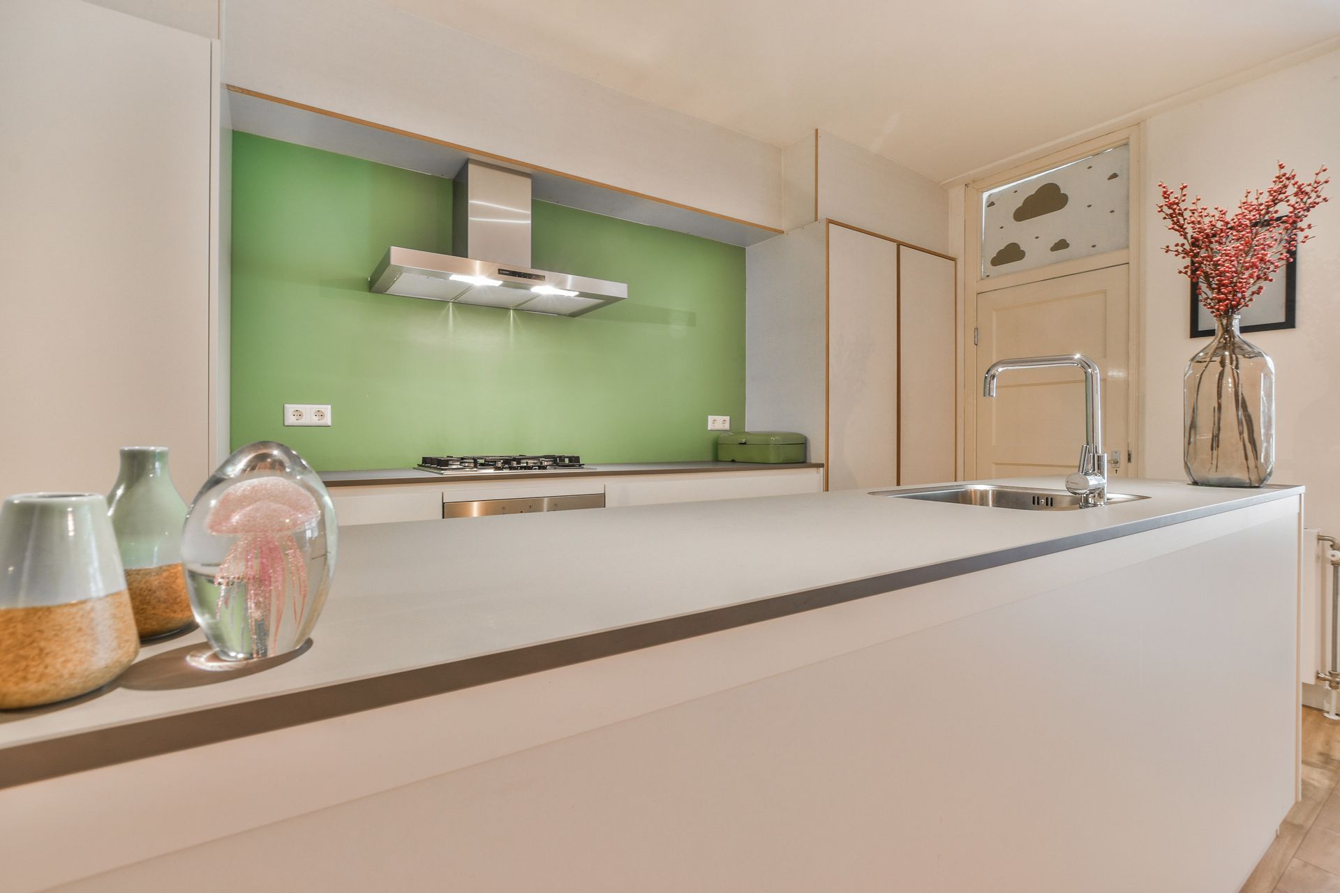 Modern kitchen with a gray countertop, green backsplash, and stainless steel hood.