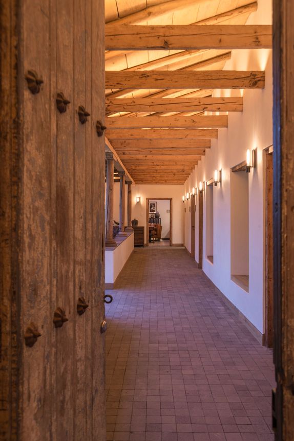 Pasillo con vigas de madera, suelo de ladrillo, apliques de pared y puertas de madera en un cálido pasillo interior.