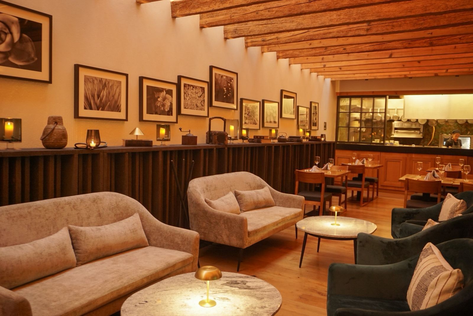 Salón cálido y con iluminación tenue, con sillones beige y oscuros, mesas pequeñas, cuadros y paredes revestidas de madera.