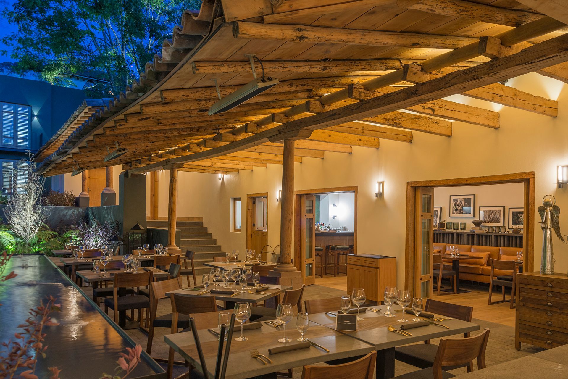 Terraza de restaurante al aire libre con mesas de madera, luces cálidas y techo de paja al atardecer.