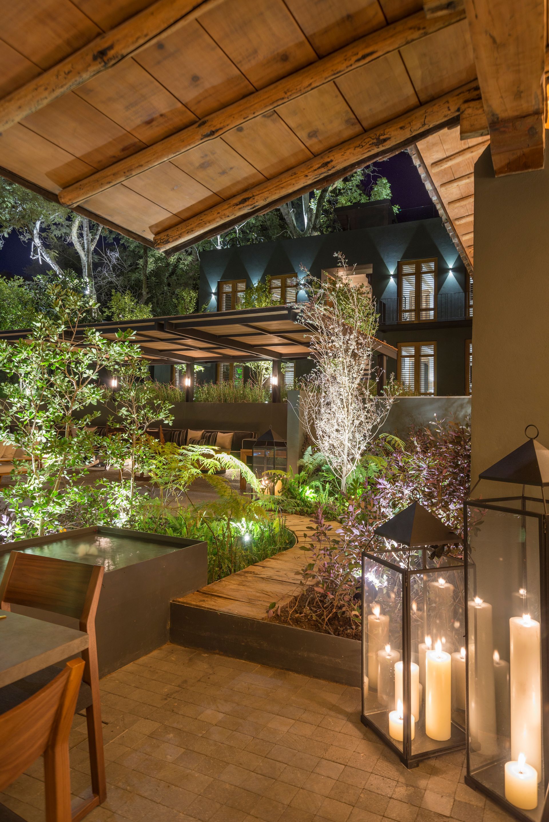 Acogedor patio por la noche con faroles brillantes, plantas y un patio interior iluminado más allá.