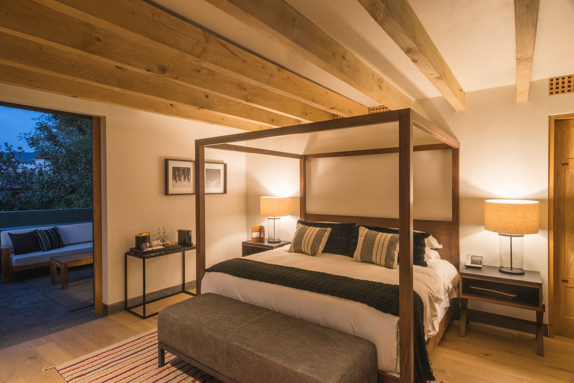Habitación acogedora con cama con dosel, iluminación cálida, vigas vistas y vistas a un patio exterior.