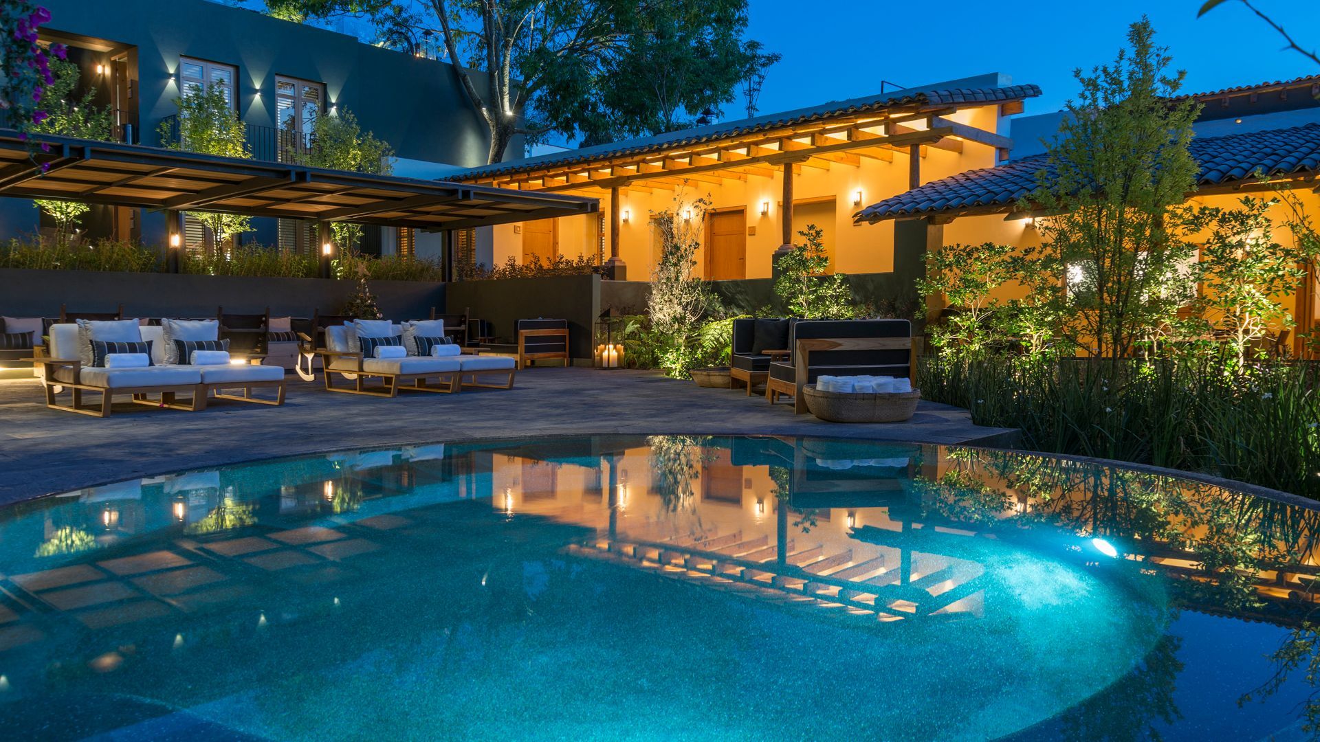 Casa de lujo moderna al atardecer con luces de patio brillantes y una piscina azul que refleja la casa.