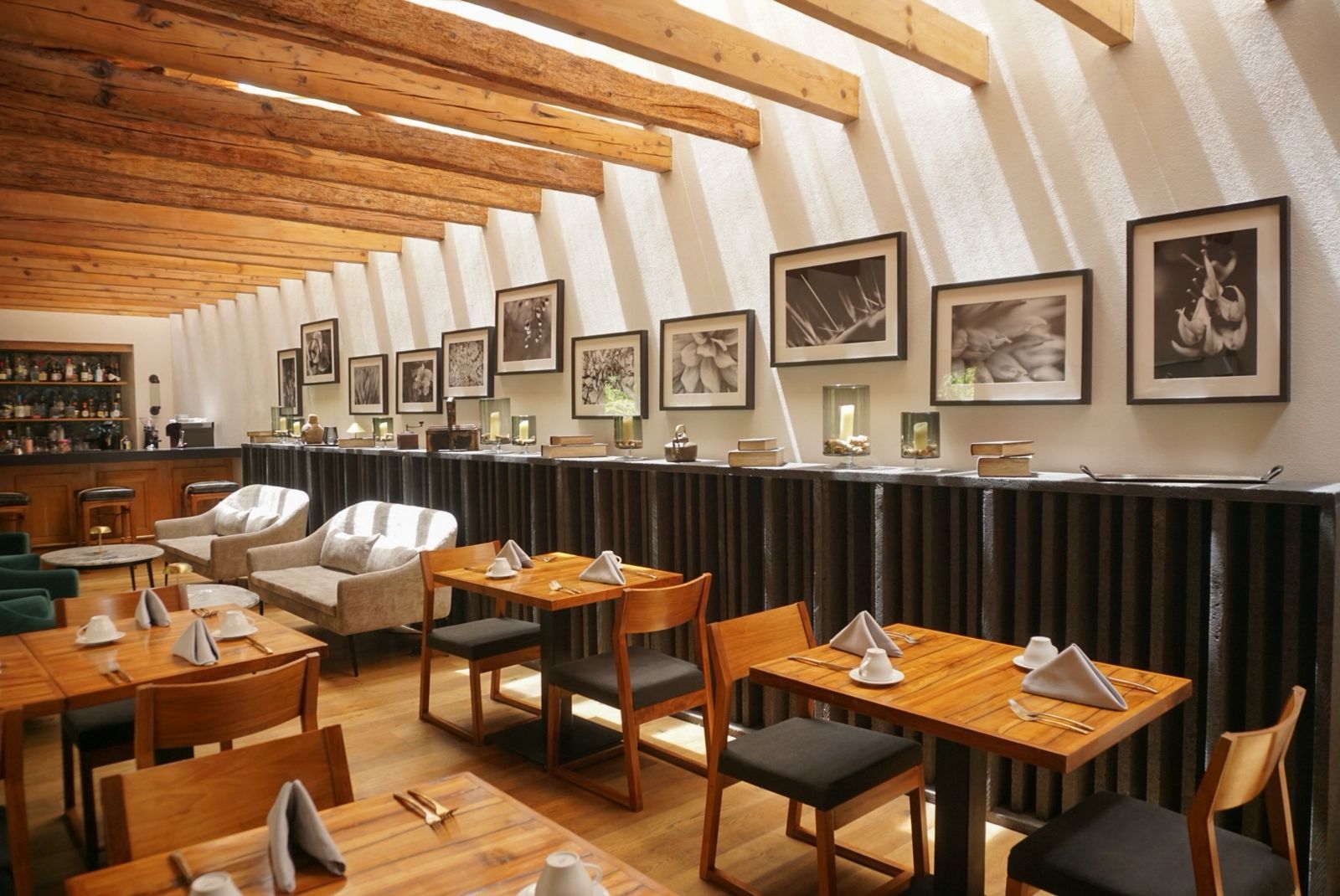 Acogedor comedor de restaurante con mesas de madera, sillas blancas, cuadros enmarcados y techo inclinado con vigas.