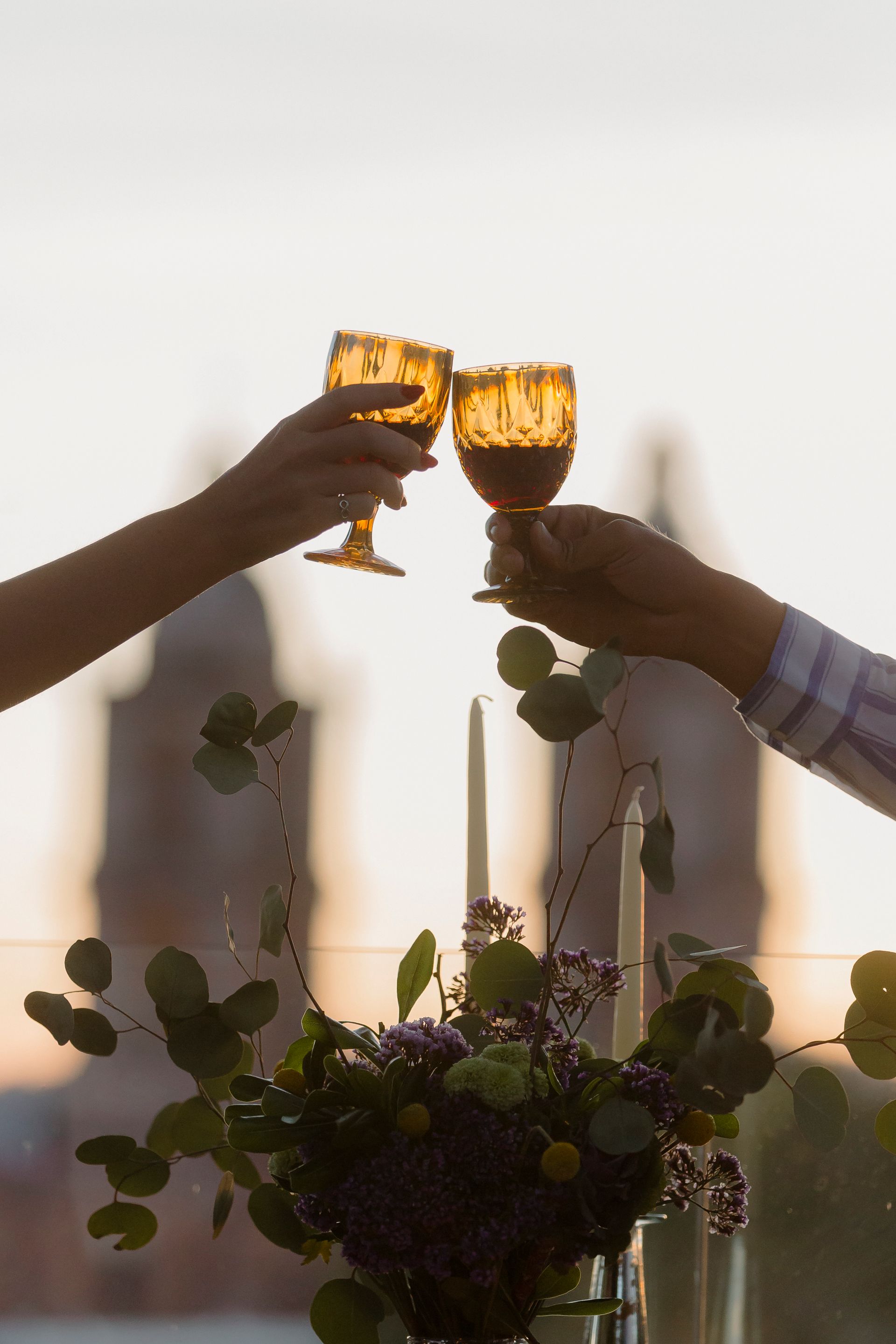 Dos manos brindando con copas de ámbar en un centro de mesa floral iluminado con velas.