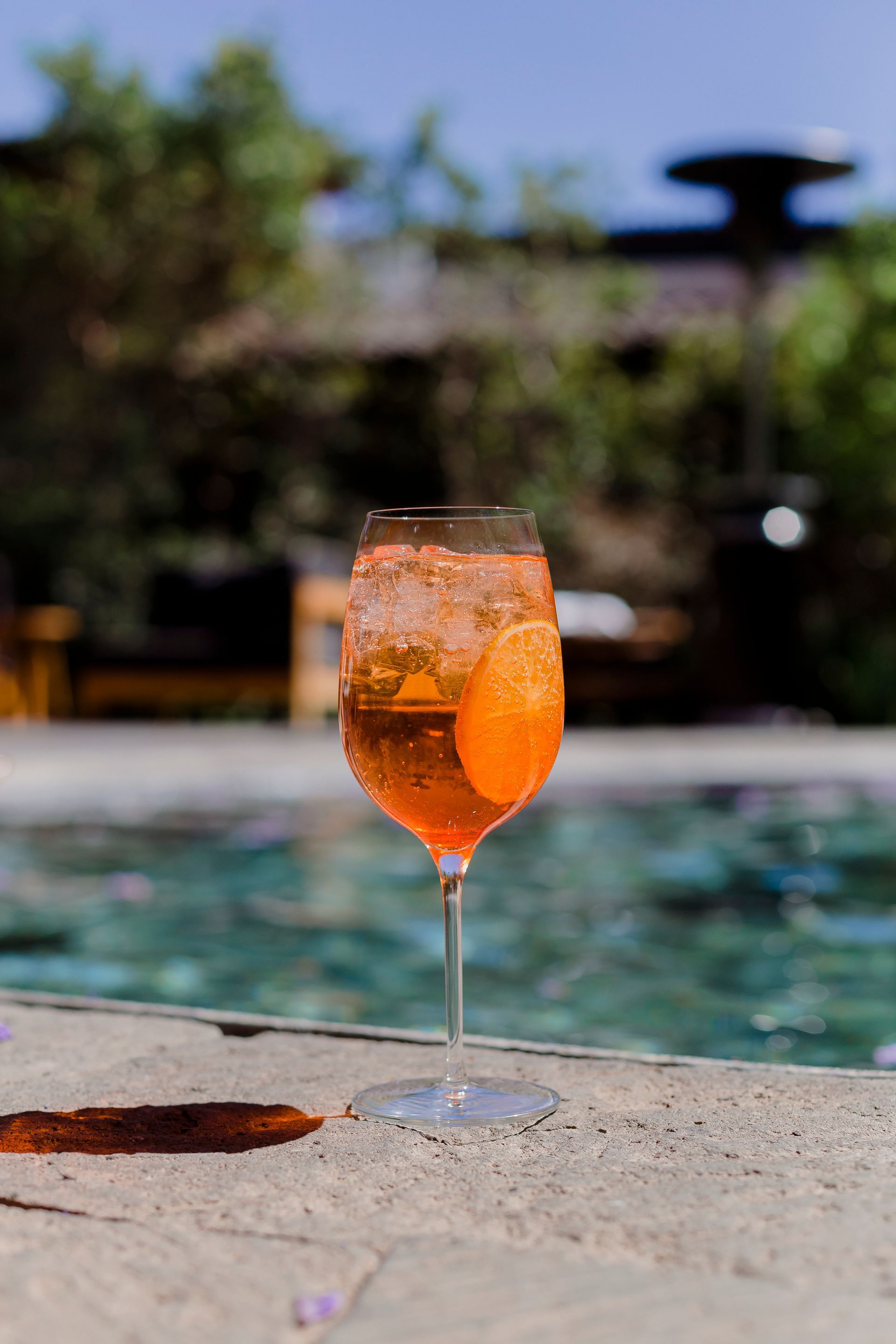 Cóctel de naranja en una copa de tallo junto a una piscina con un patio exterior borroso de fondo.