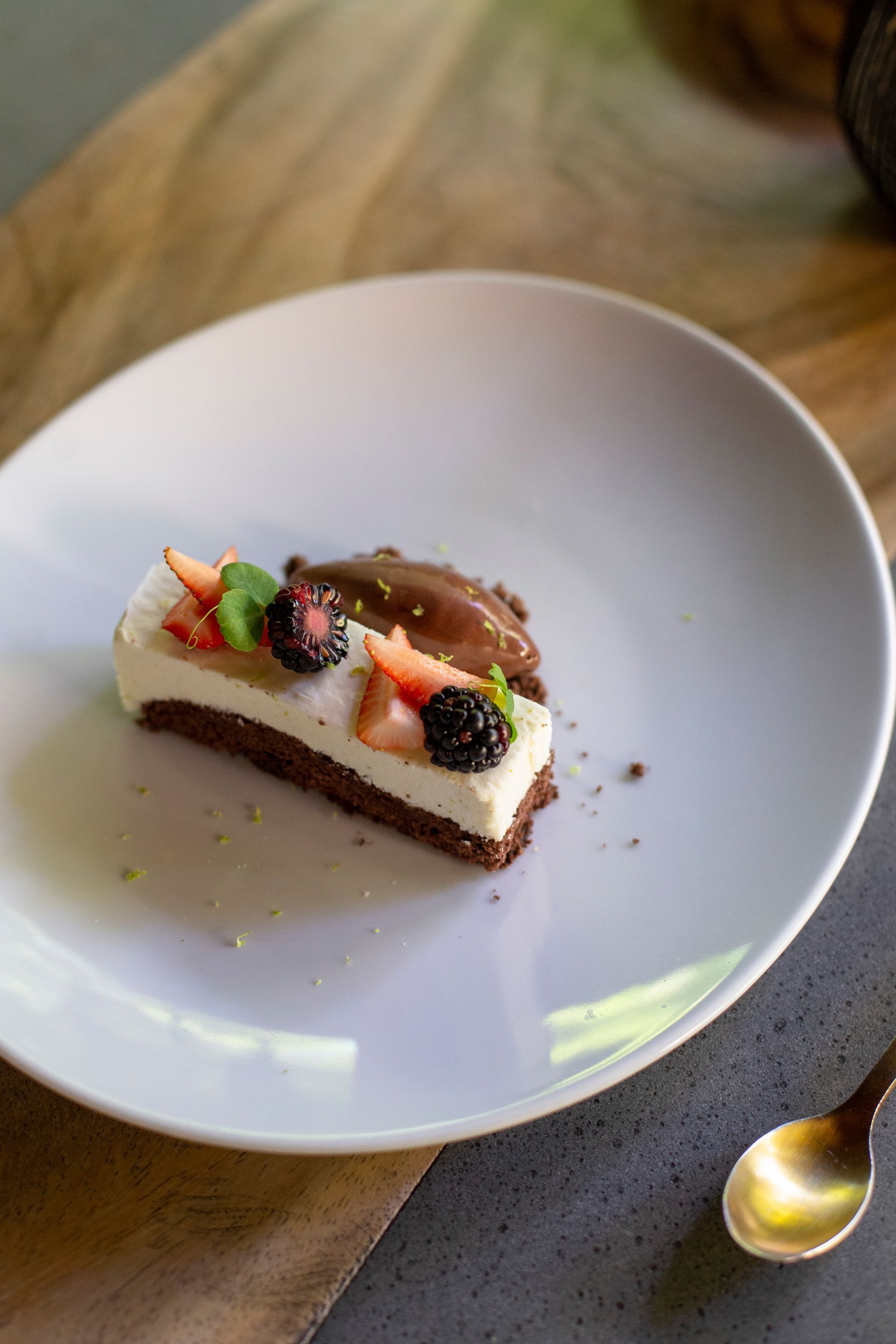 Una porción de tarta de queso con fresas sobre un plato blanco con una cuchara dorada al lado.