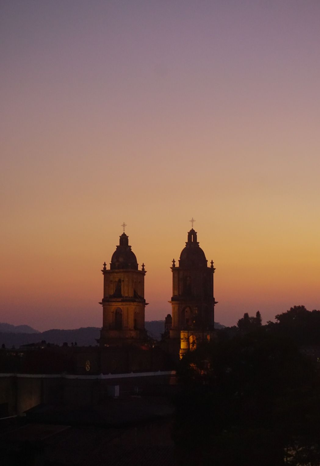 Torres de catedral recortadas contra el cielo rosado-anaranjado al atardecer.