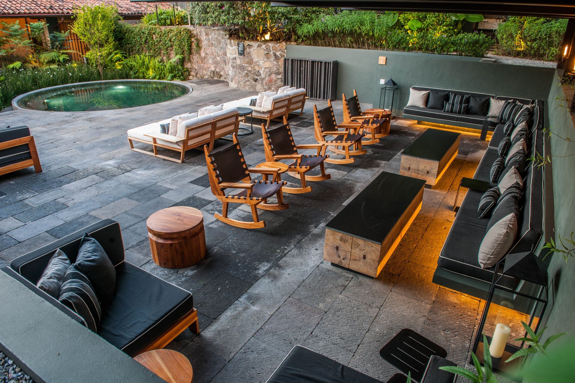Patio exterior moderno con sofás modulares, mecedoras, fogata y piscina.