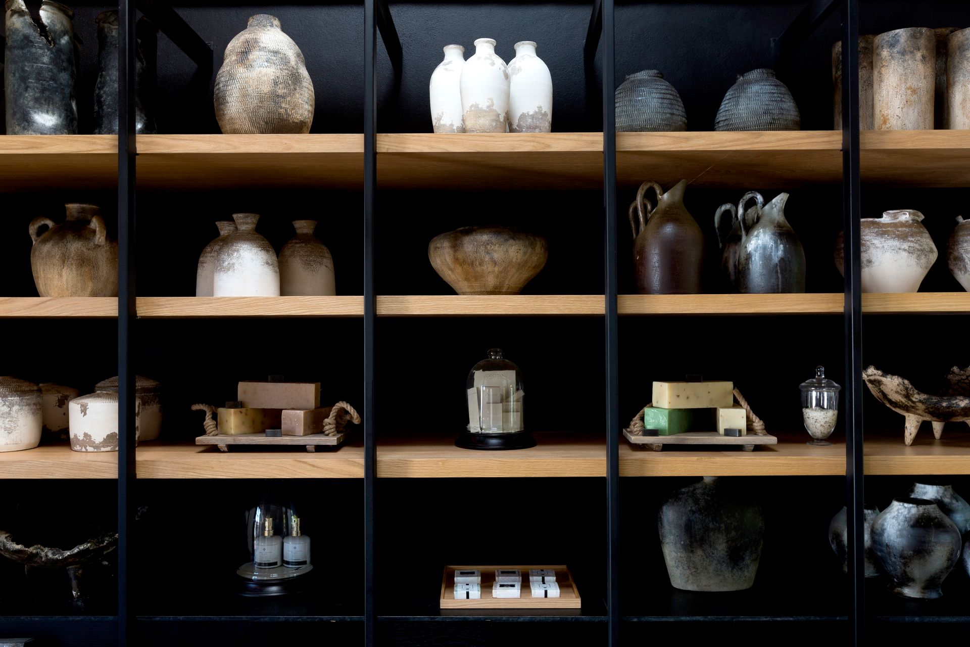 Colección de cerámica, jarrones, teteras y pequeños objetos decorativos expuestos en una vitrina oscura.