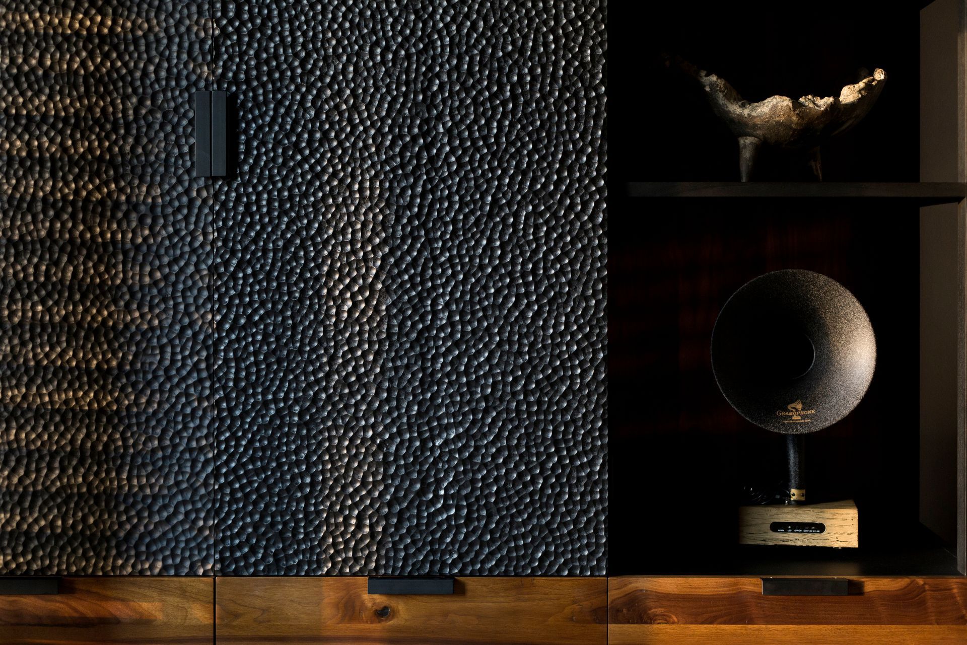 Pared oscura con textura y estantes que sostienen una figurita de pájaro y un globo terráqueo sobre una mesa de madera.