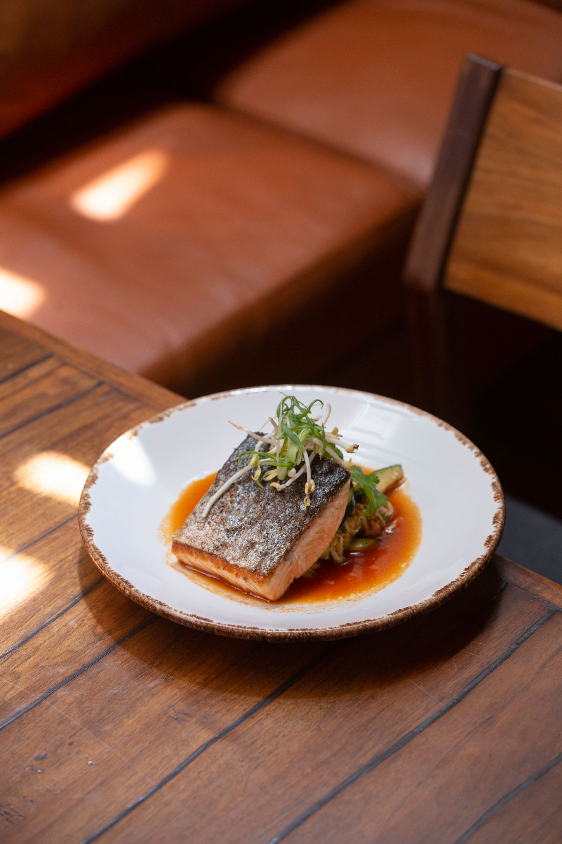 Pescado sellado al plato con hierbas en salsa sobre una mesa de restaurante de madera.