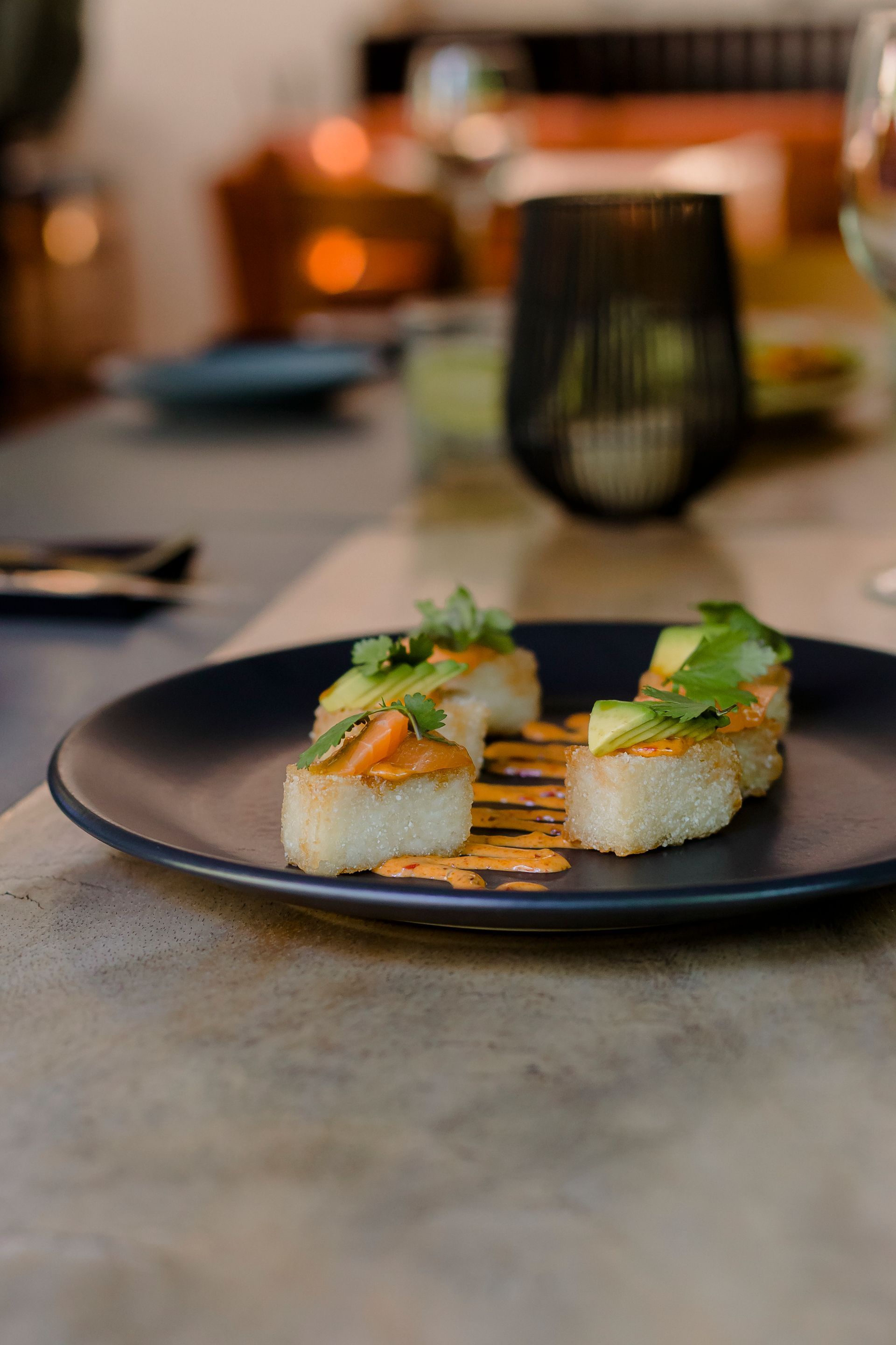 Aperitivo gourmet emplatado en una mesa de restaurante, con el comedor difuminado al fondo.