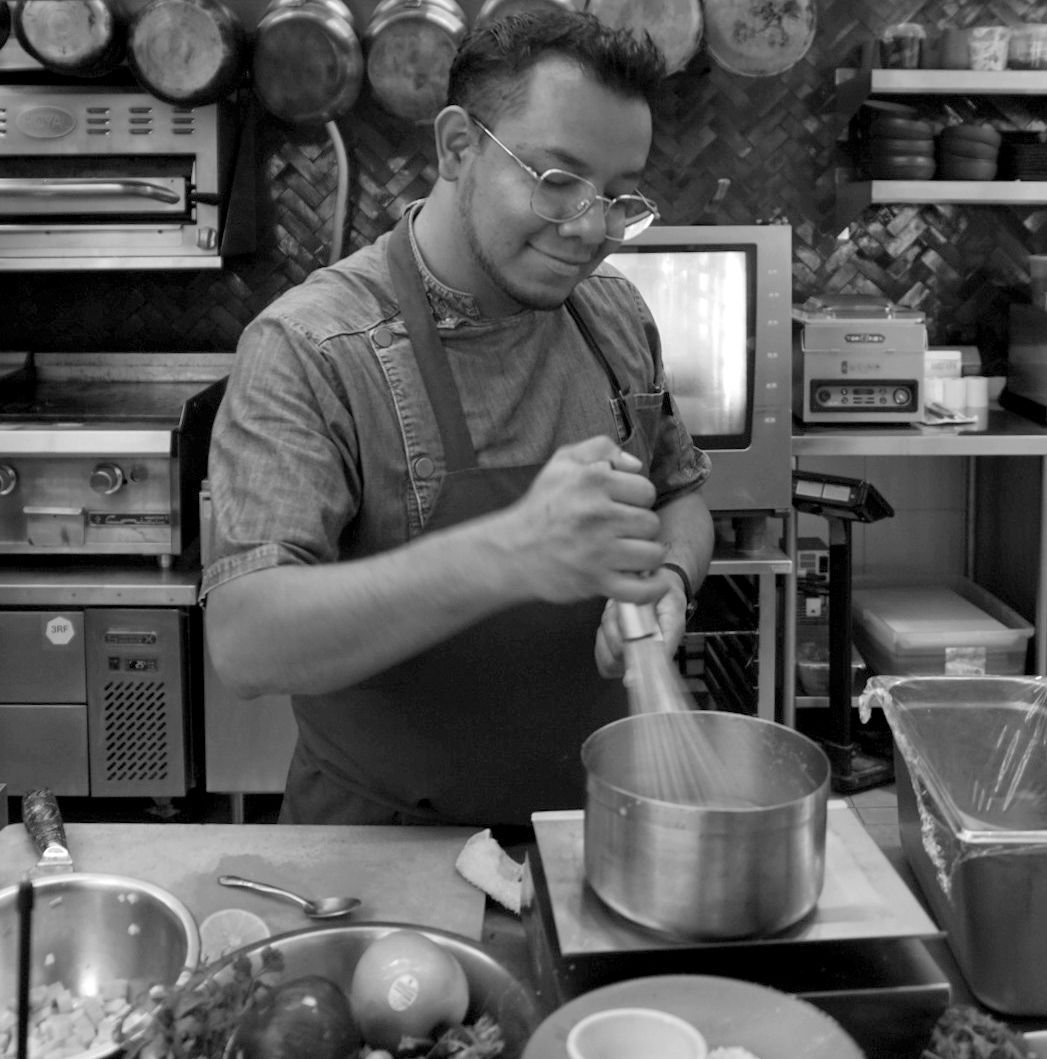 Un chef remueve una olla en la cocina, con los ingredientes y utensilios sobre la encimera.