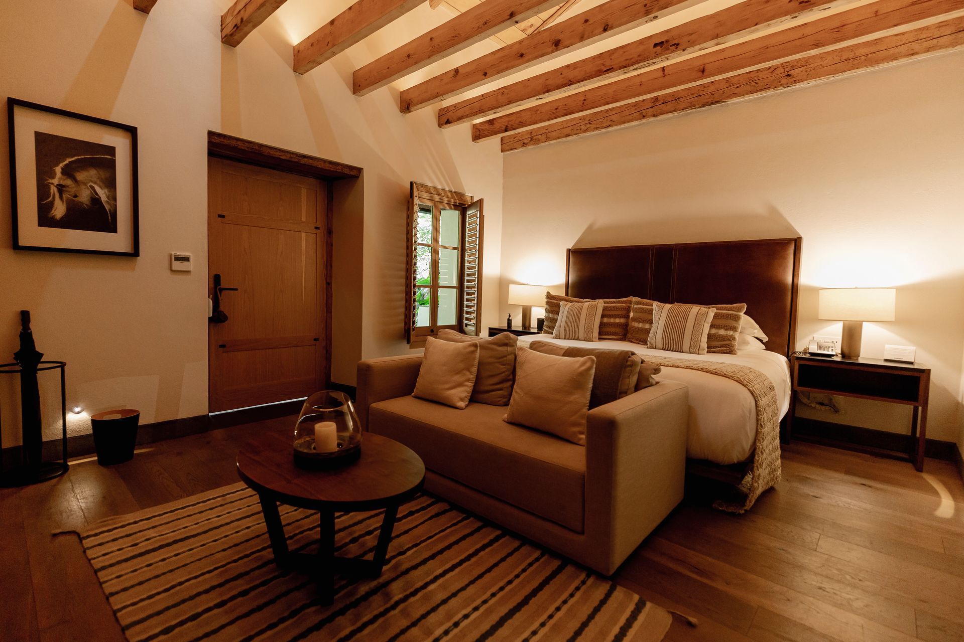 Habitación acogedora con cama, sofá, vigas de madera e iluminación cálida.