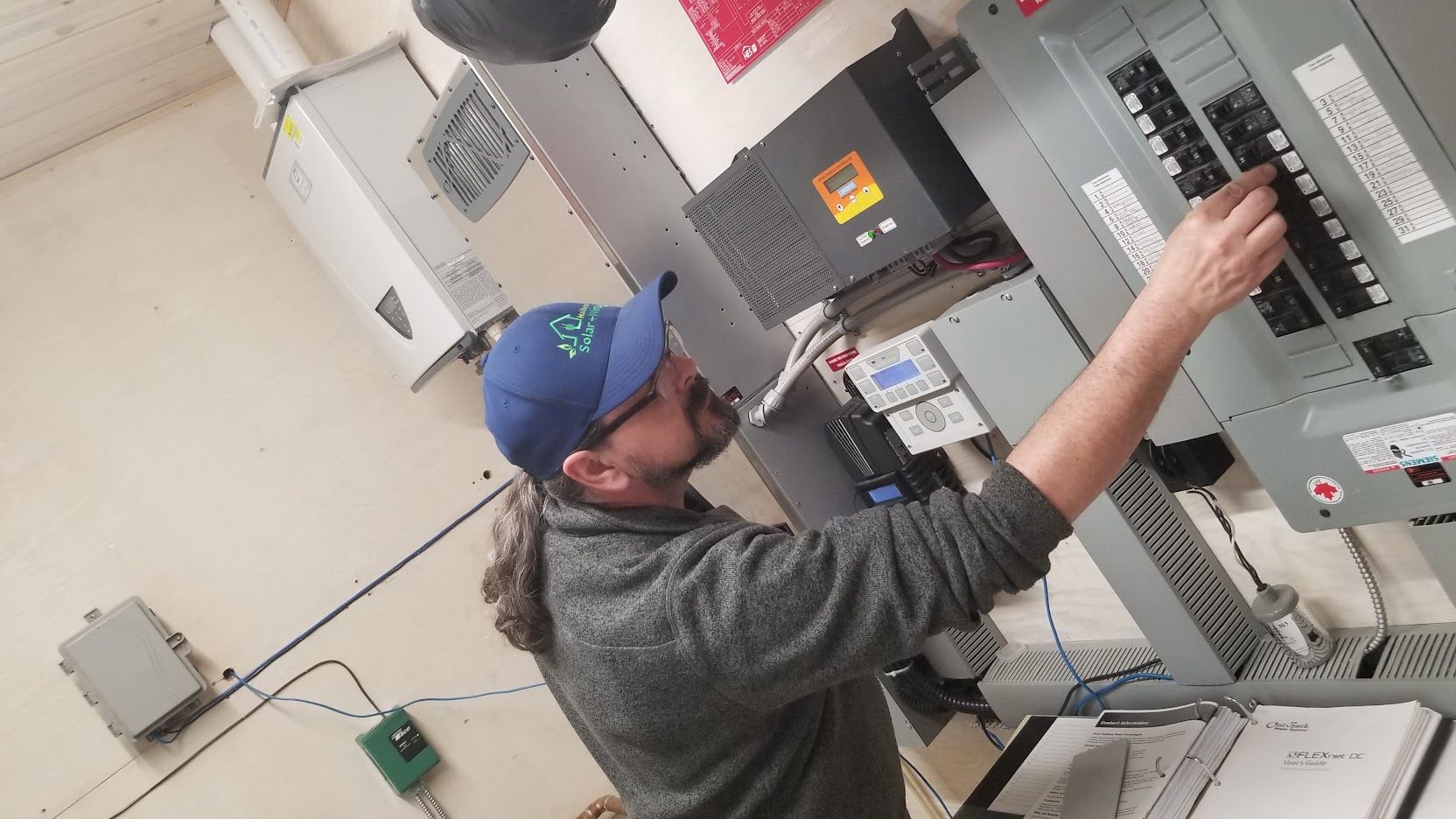 A man in a blue hat is working on an electrical box.