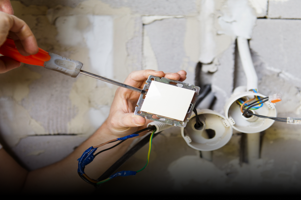 A person is fixing a light switch with a screwdriver.
