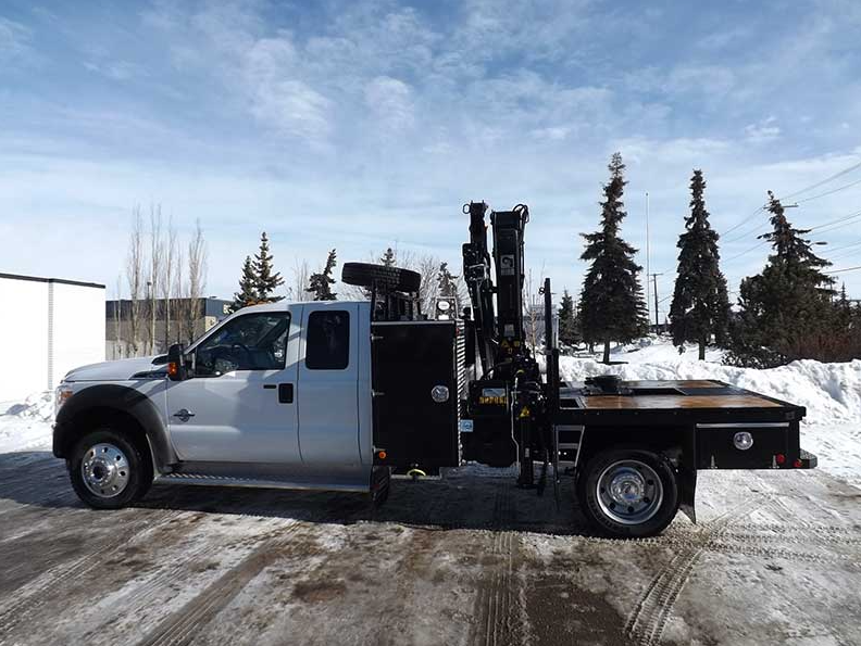 Camion de travail argenté avec grue noire par temps de neige.