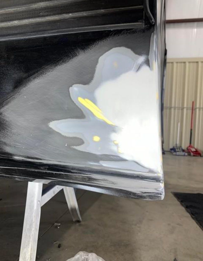 A car's painted surface is being repaired with filler; white and gray patches visible. Black bottom edge on a stand.