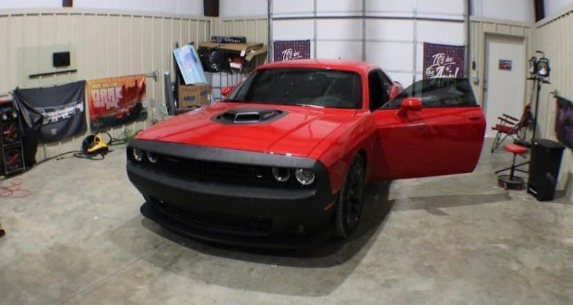 Red Dodge Challenger with open door inside a garage.