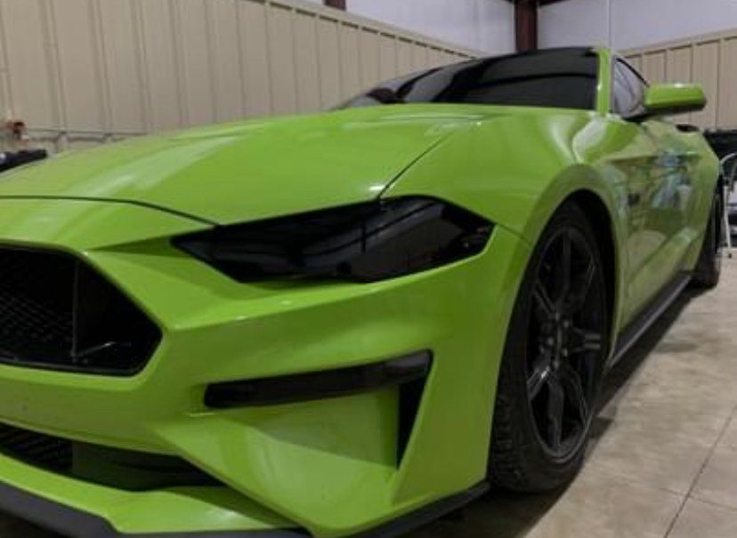 Lime green Ford Mustang with black wheels and tinted headlights parked indoors.