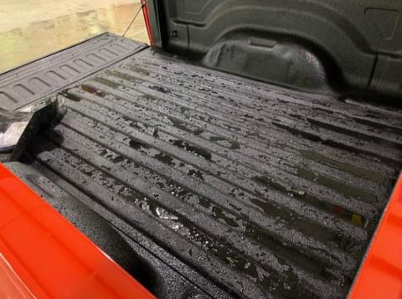 Black truck bed with wet surface, orange side, in indoor setting.