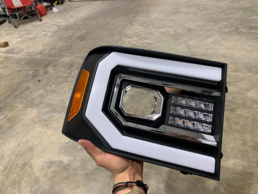 Black and chrome truck headlight with bright white LED accents and amber turn signal, held in hand.