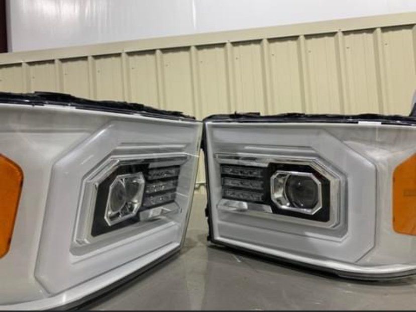Two custom car headlights, white with black accents and orange turn signals, sit side by side.