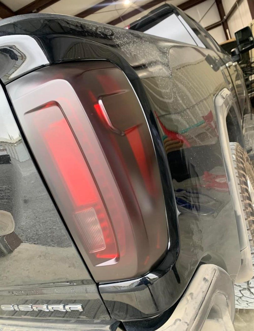 Black pickup truck's taillight with tinted cover, showing red lights.