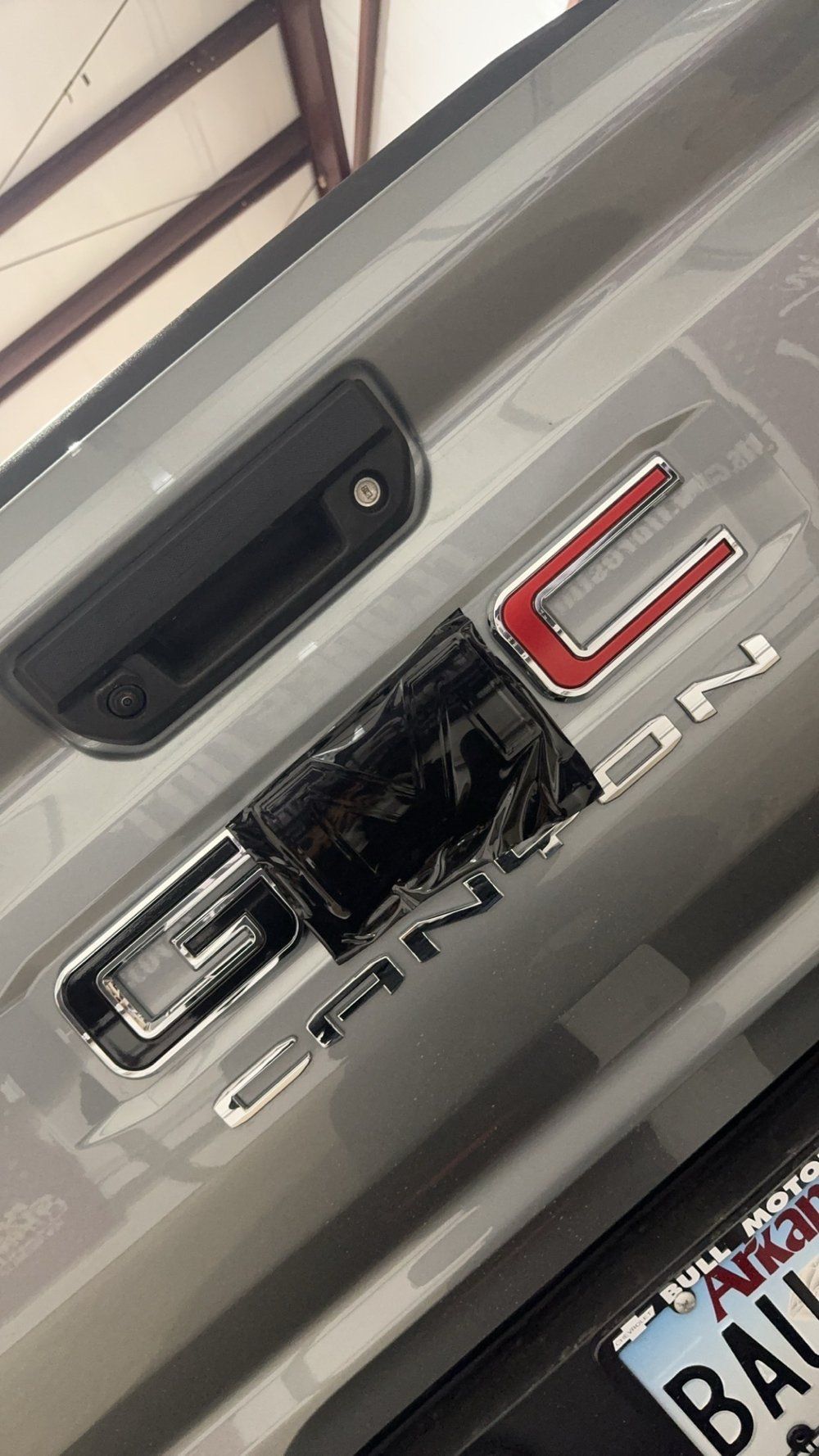 Gray GMC Canyon tailgate with black door handle and logo partially covered in black tape.
