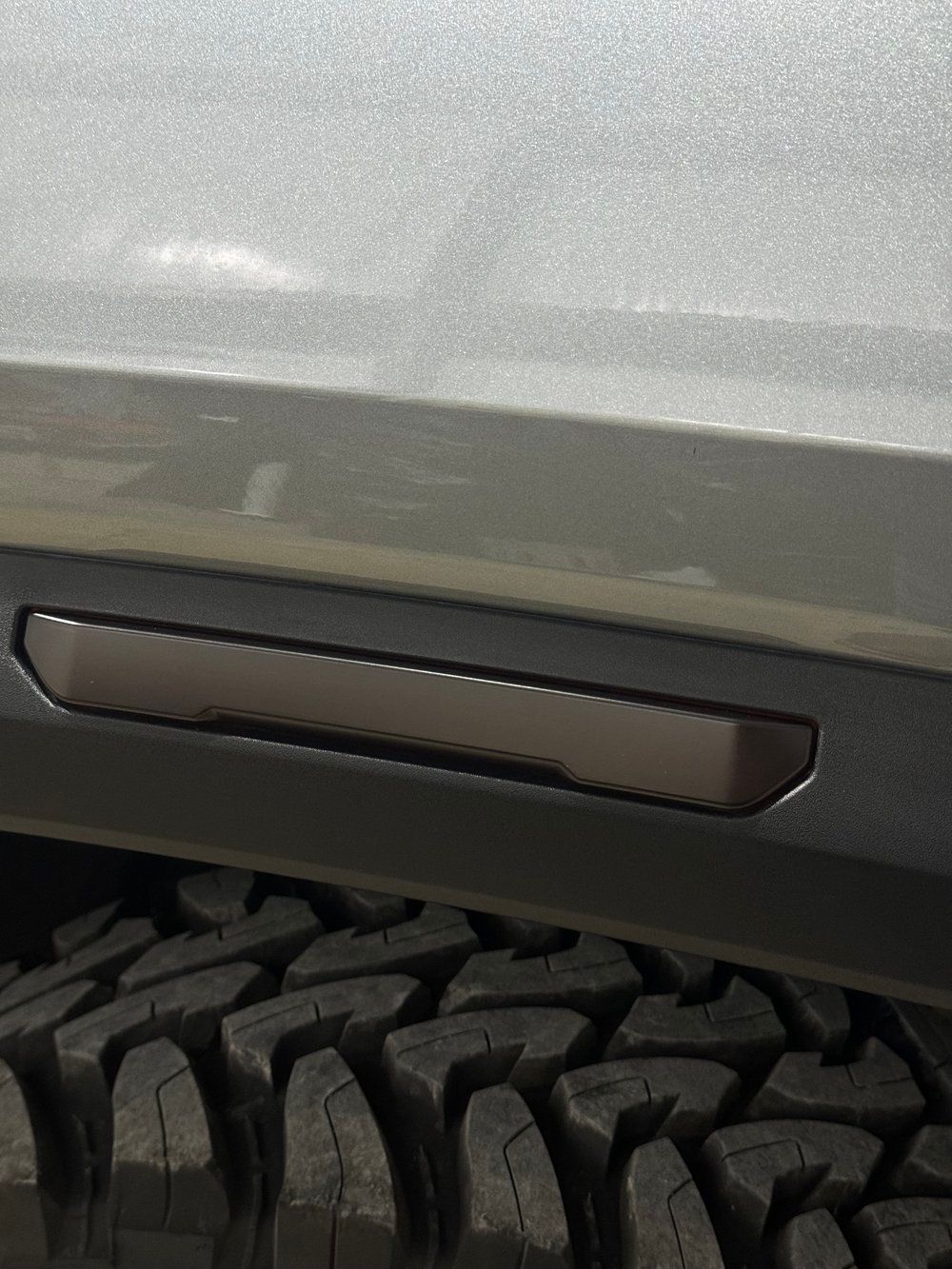 Dark brown side marker light on a gray vehicle near a black tire.