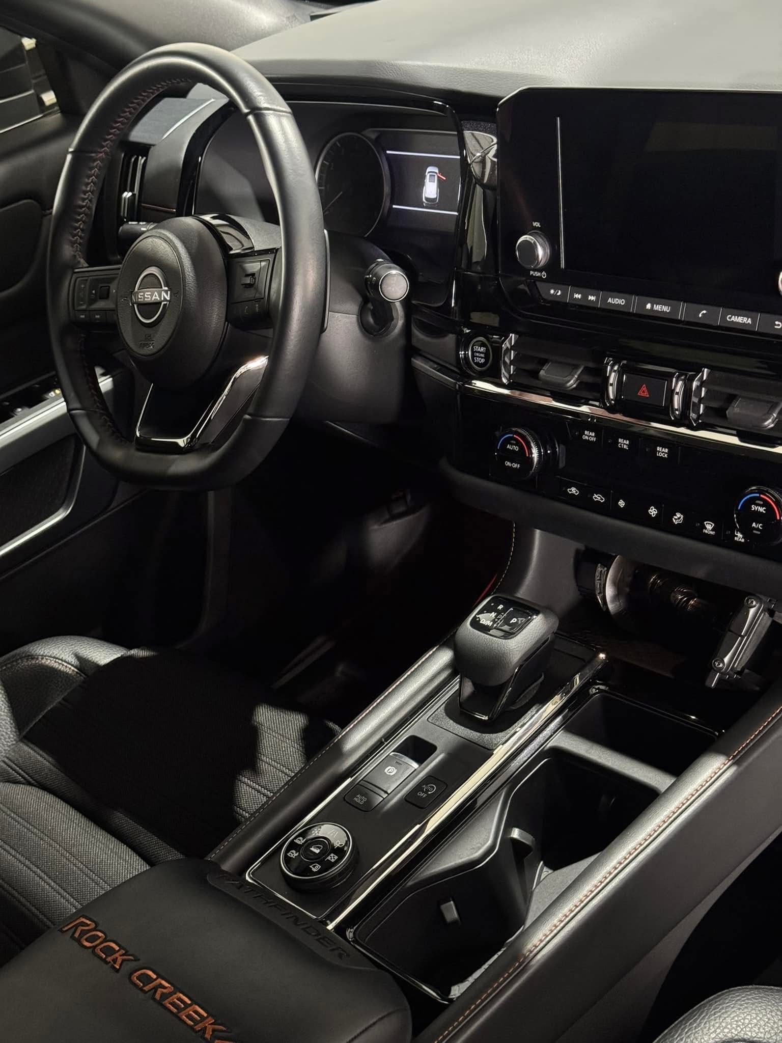 Black Nissan car interior with steering wheel, dashboard, and gear shift visible.