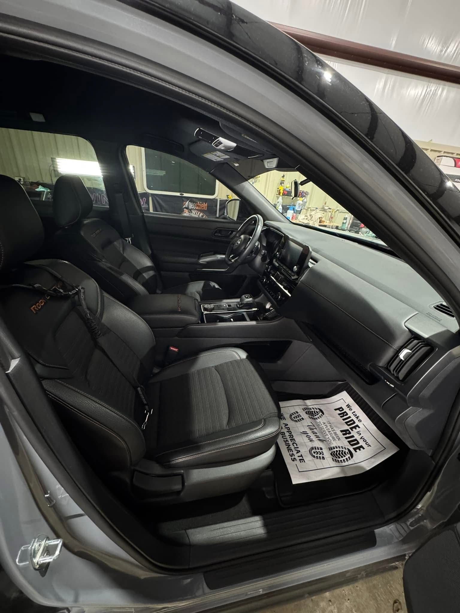 Interior view of a gray car with black seats and a paper on the floor.