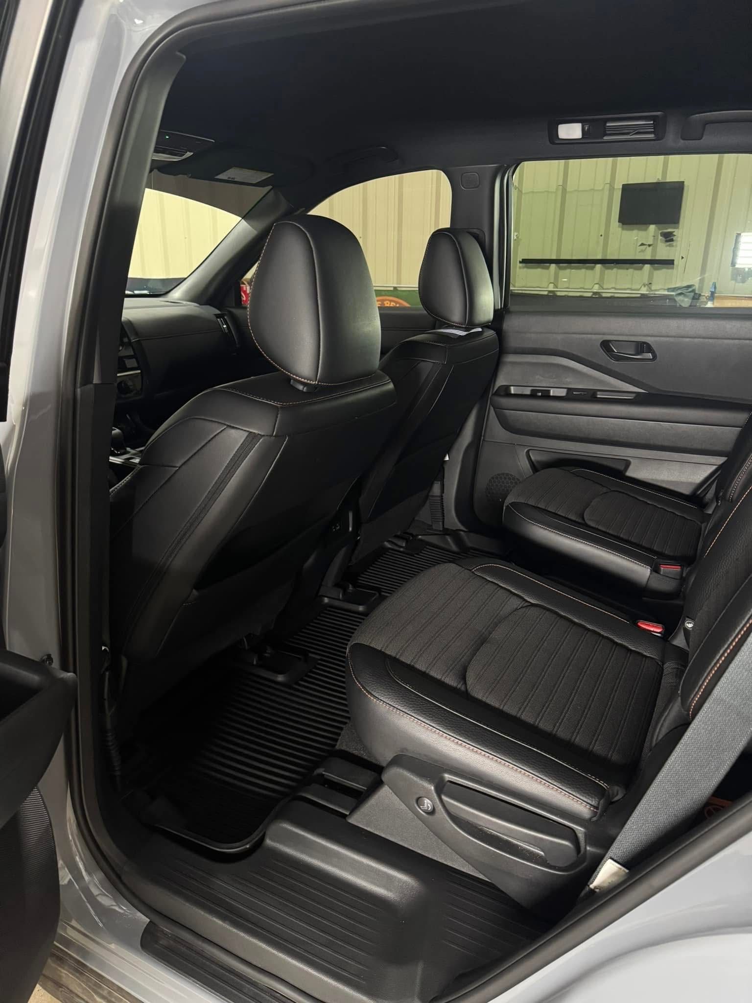 Interior view of a gray car's back seat with black leather seats, a black floor mat, and a window.
