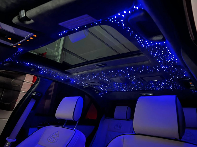 Car interior with blue starry LED lights on the ceiling, over white seats and a sunroof.