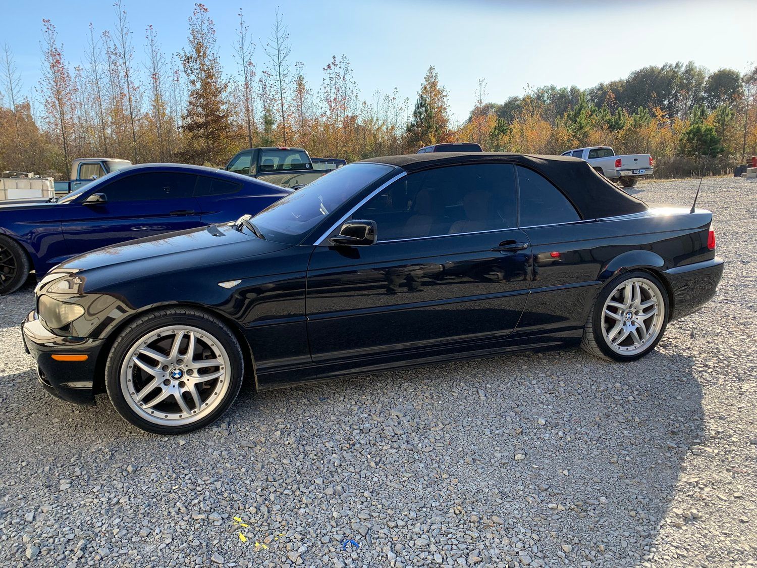 Black convertible car parked on gravel, with tinted windows and silver rims.